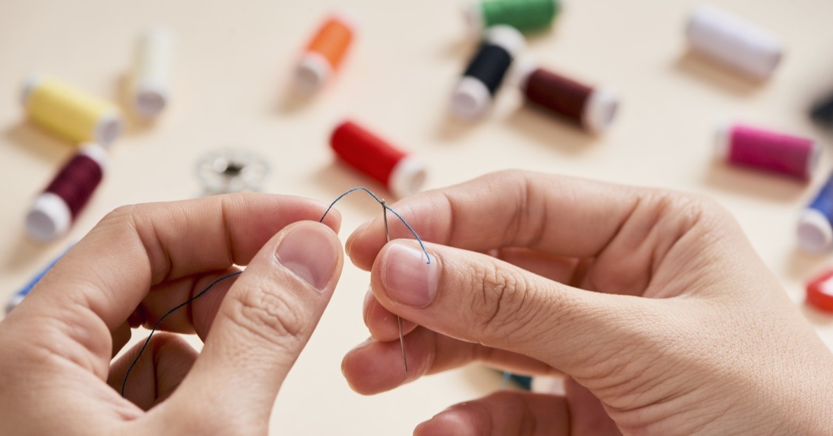 Person threading a needle with spools in the background.